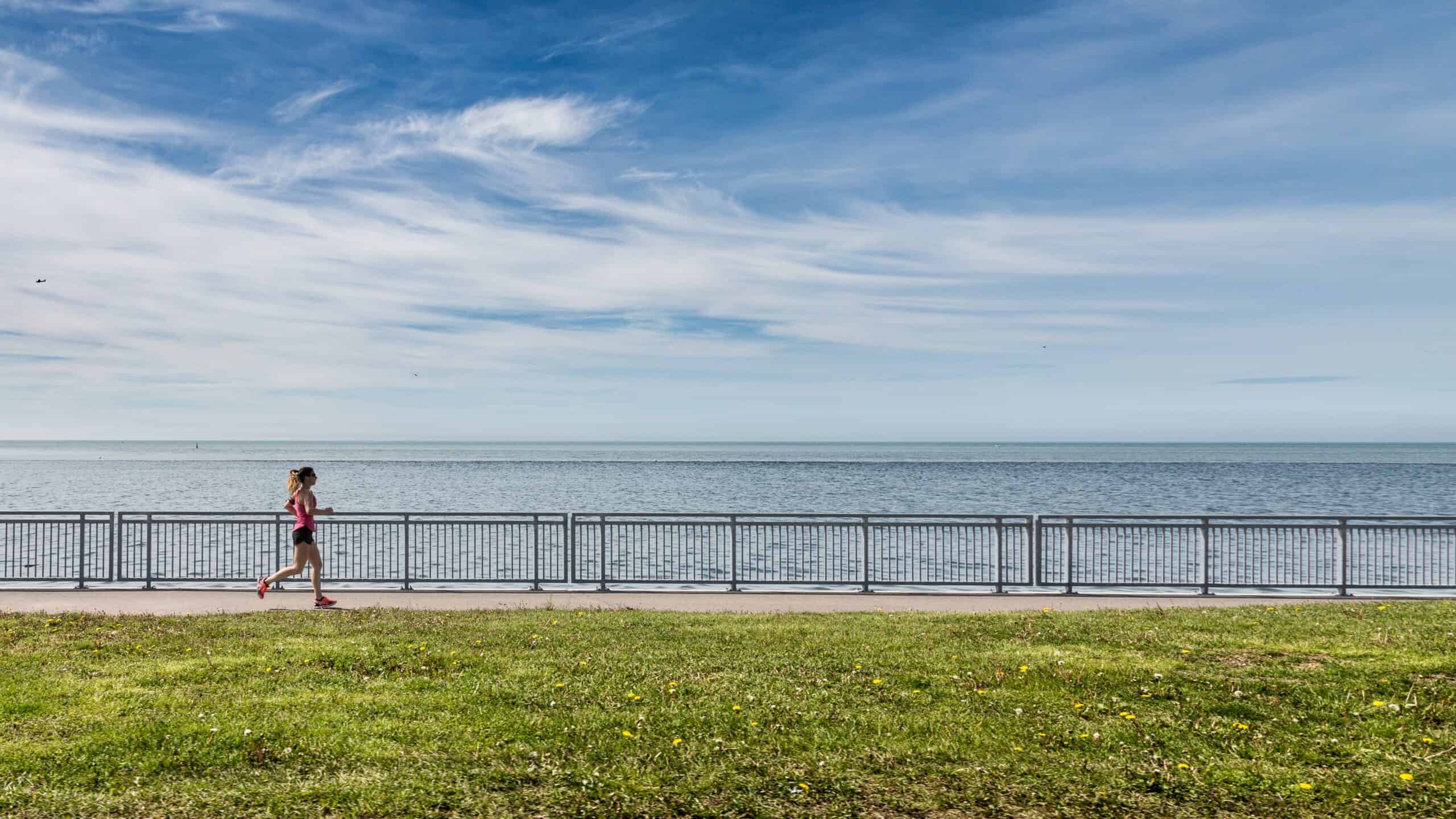 A woman running with her foot slightly in front of her flexed knee in front of a body of water.