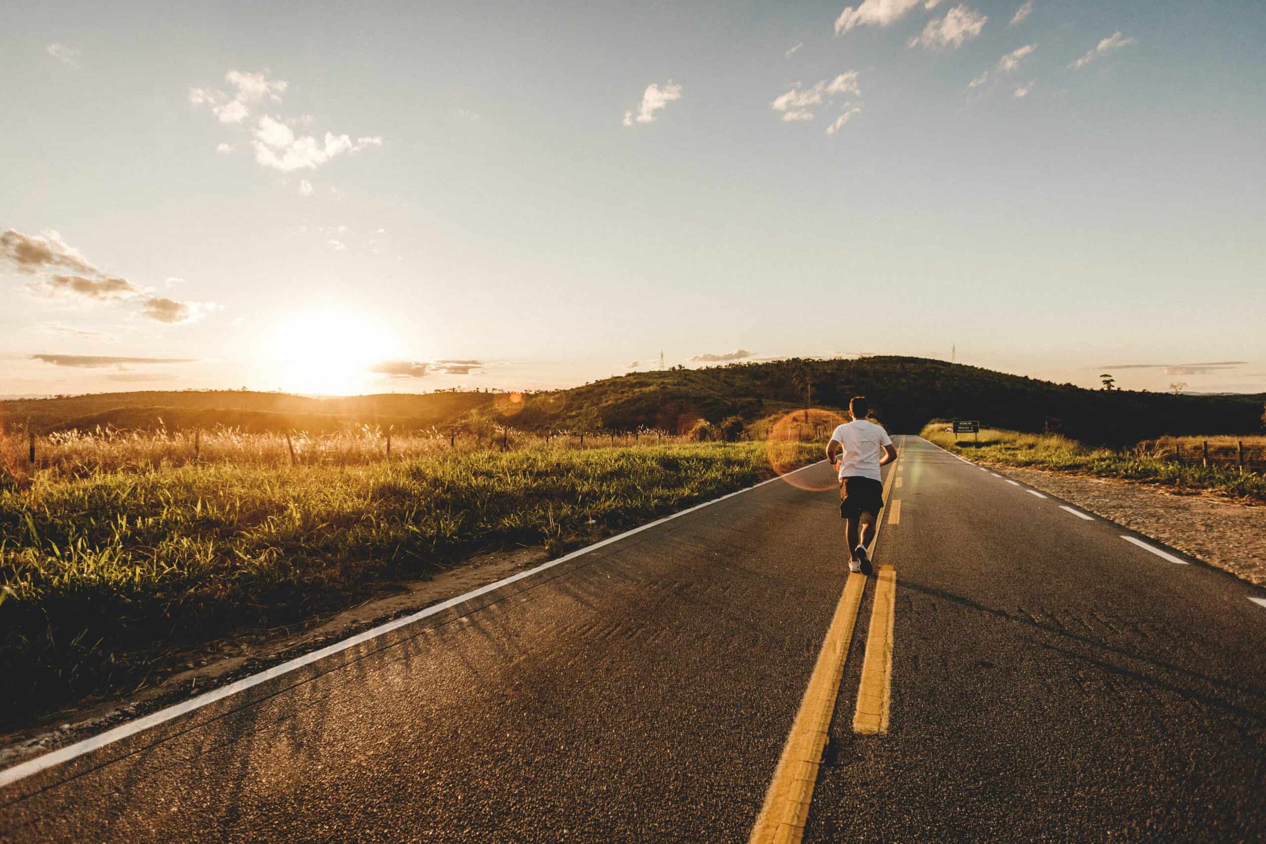 A man running on a two way street at a good running pace as the sun sets.