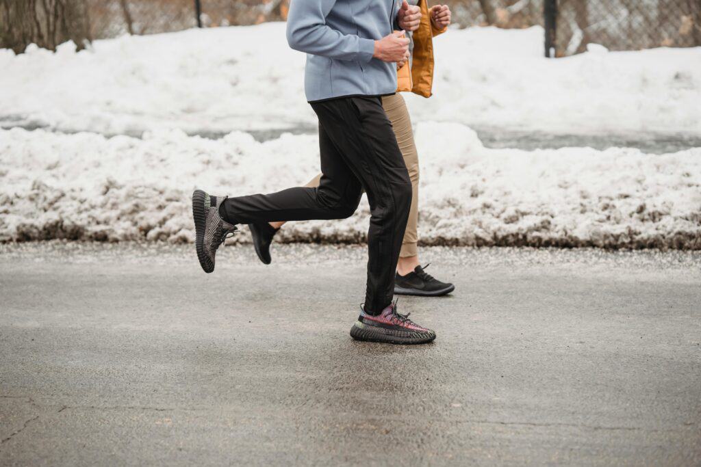 two people wearing cold weather running gear while jogging on a street with snow