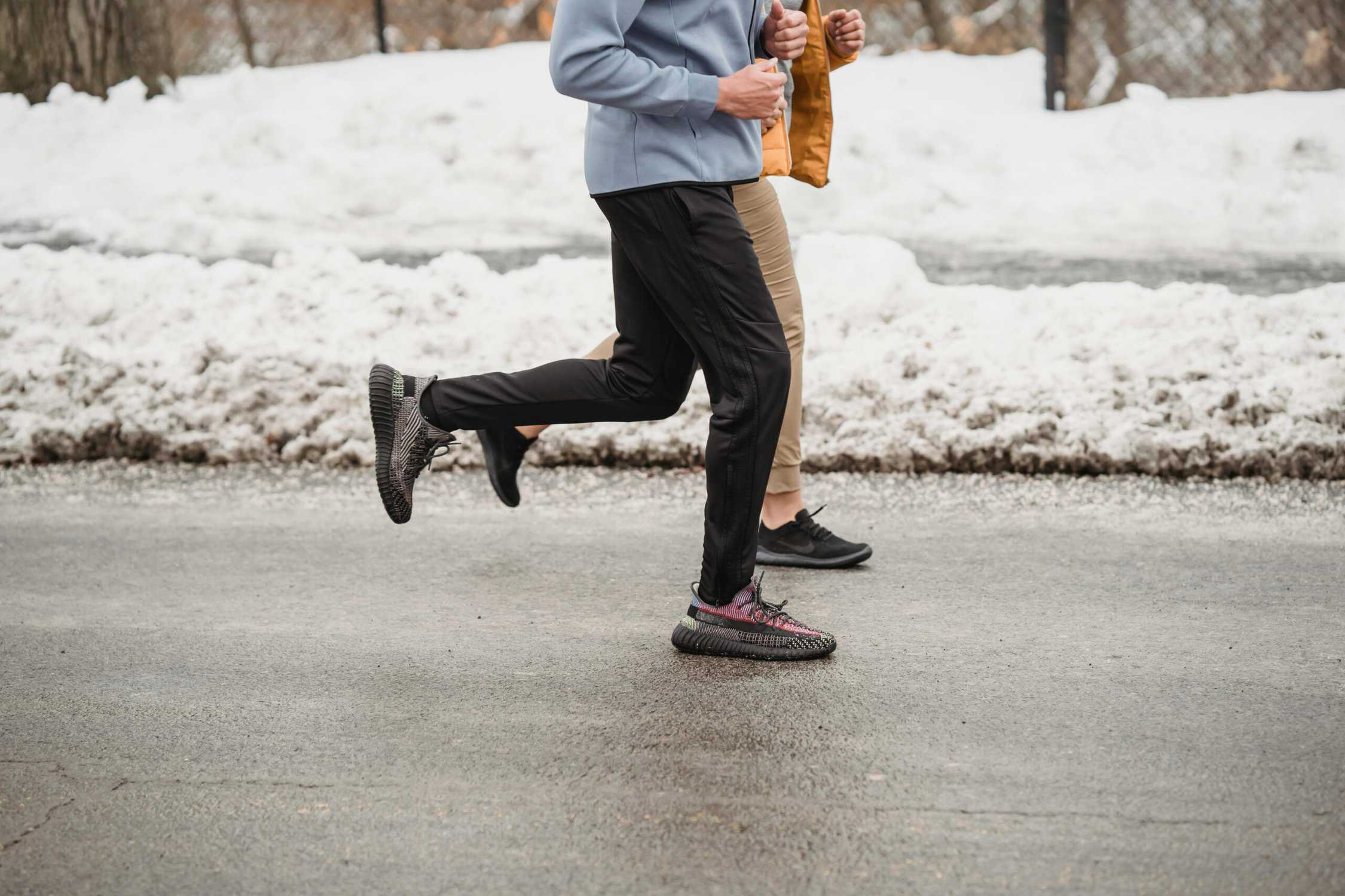 two people wearing cold weather running gear while jogging on a street with snow