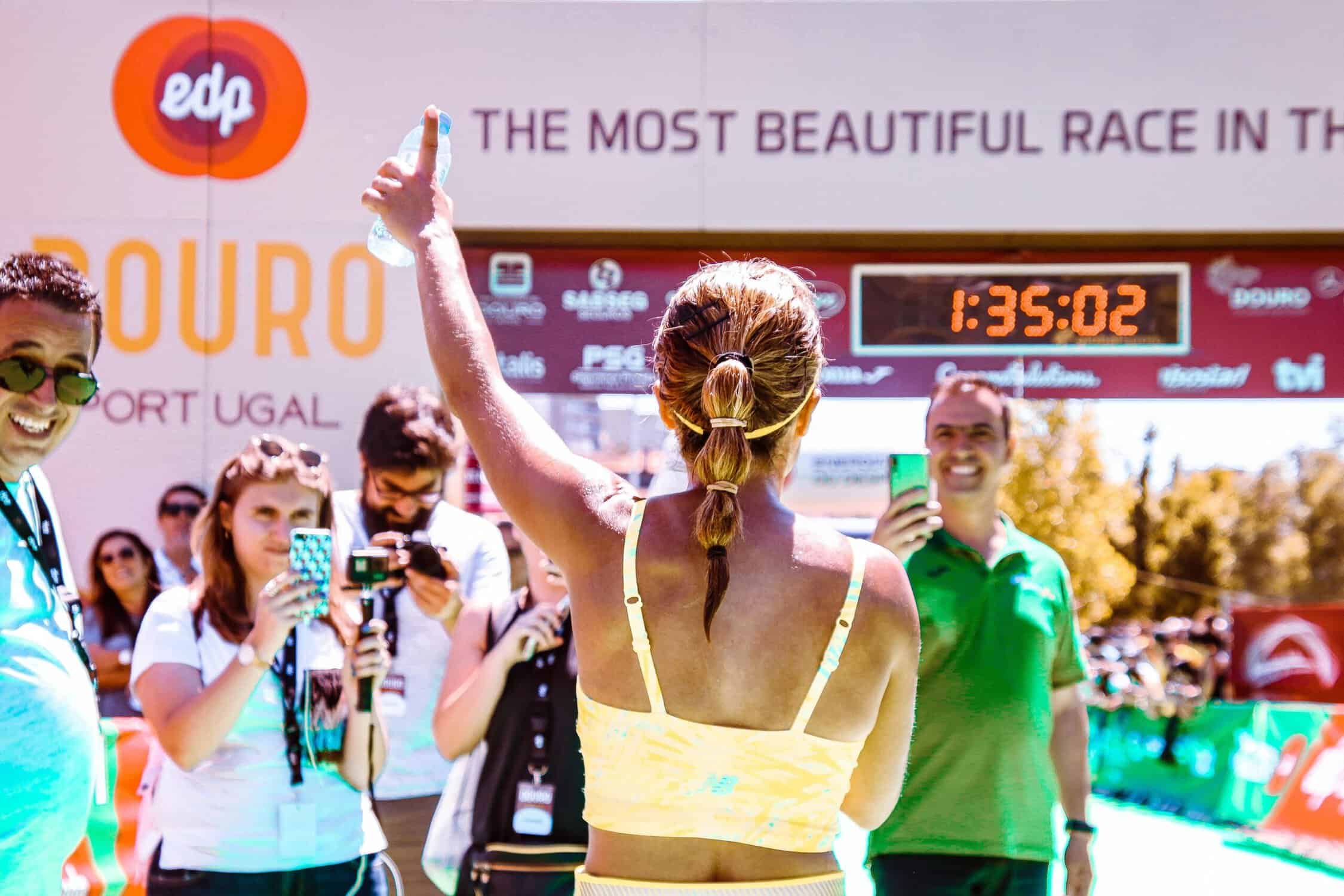 female runner at the finish line of a half marathon, holding up the number 1 finger