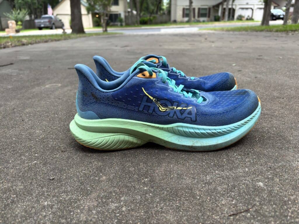 A pair of well-worn Hoka Mach 6 running shoes sitting on pavement, with a view from the side.