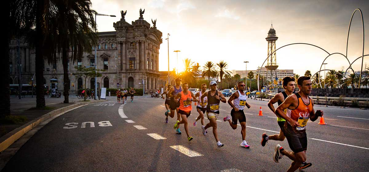 A couple of male runners with race bibs running down the street in the Mitja Marato de Barcelona half marathon.