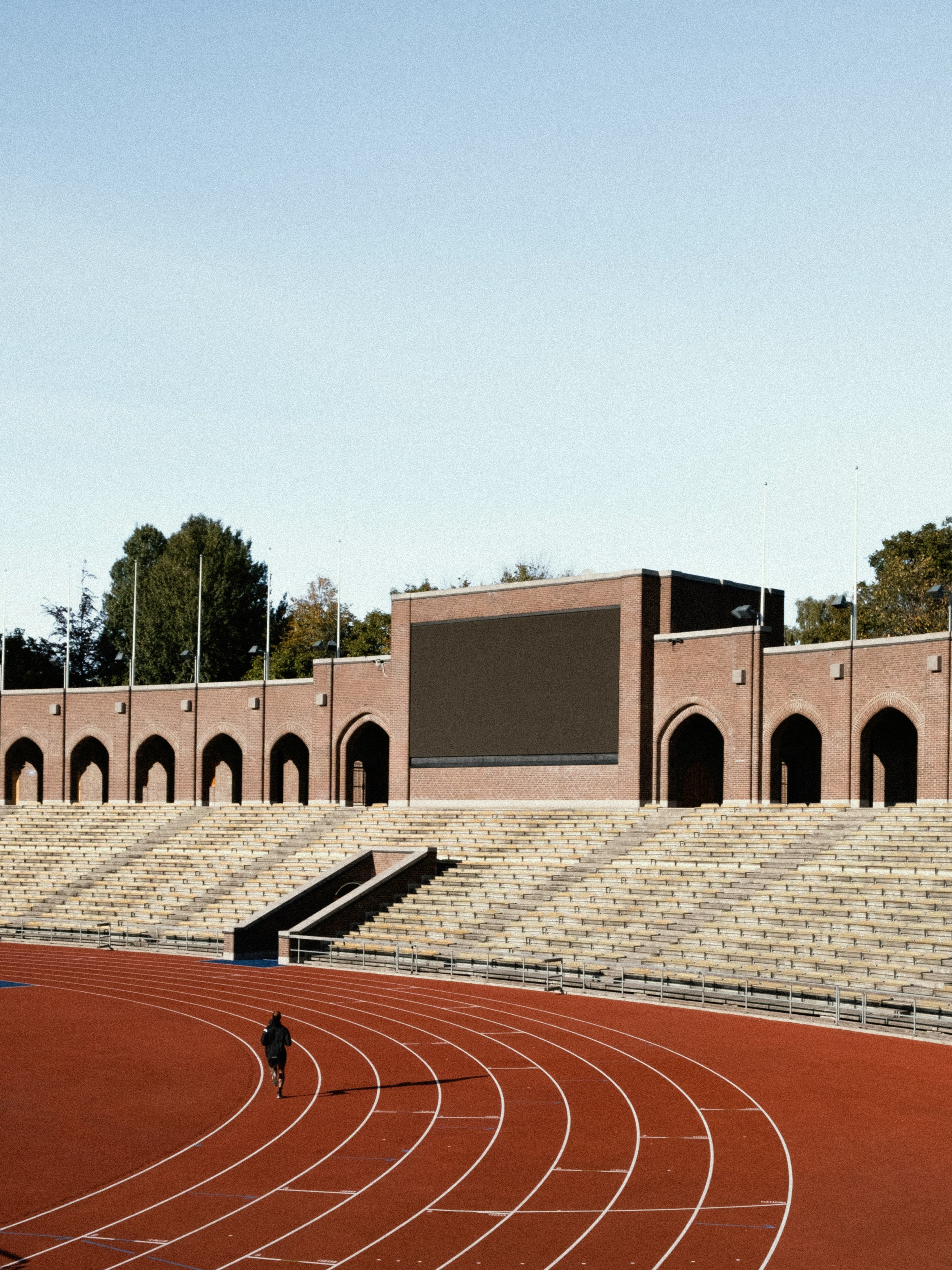 A person doing track workouts for runners at a high school with a stadium in the background.