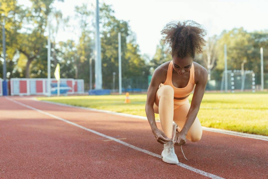 A runner on a track ready to workout, bent over tying her shoe