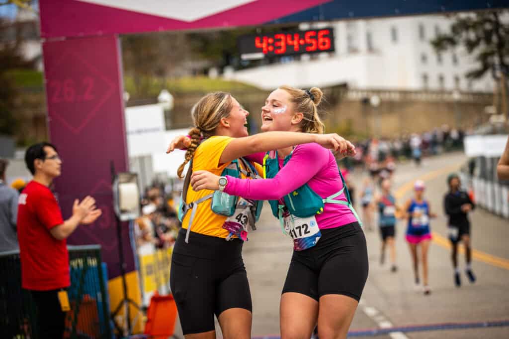 Two females at the the finish line of the Richmond Marathon, hugging. 