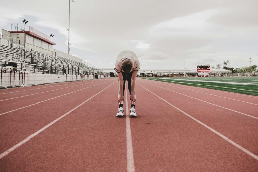 A runner after a track workout, bent over with his hands on his shins, tired.