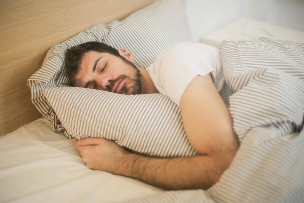 man sleeping soundly on striped sheets