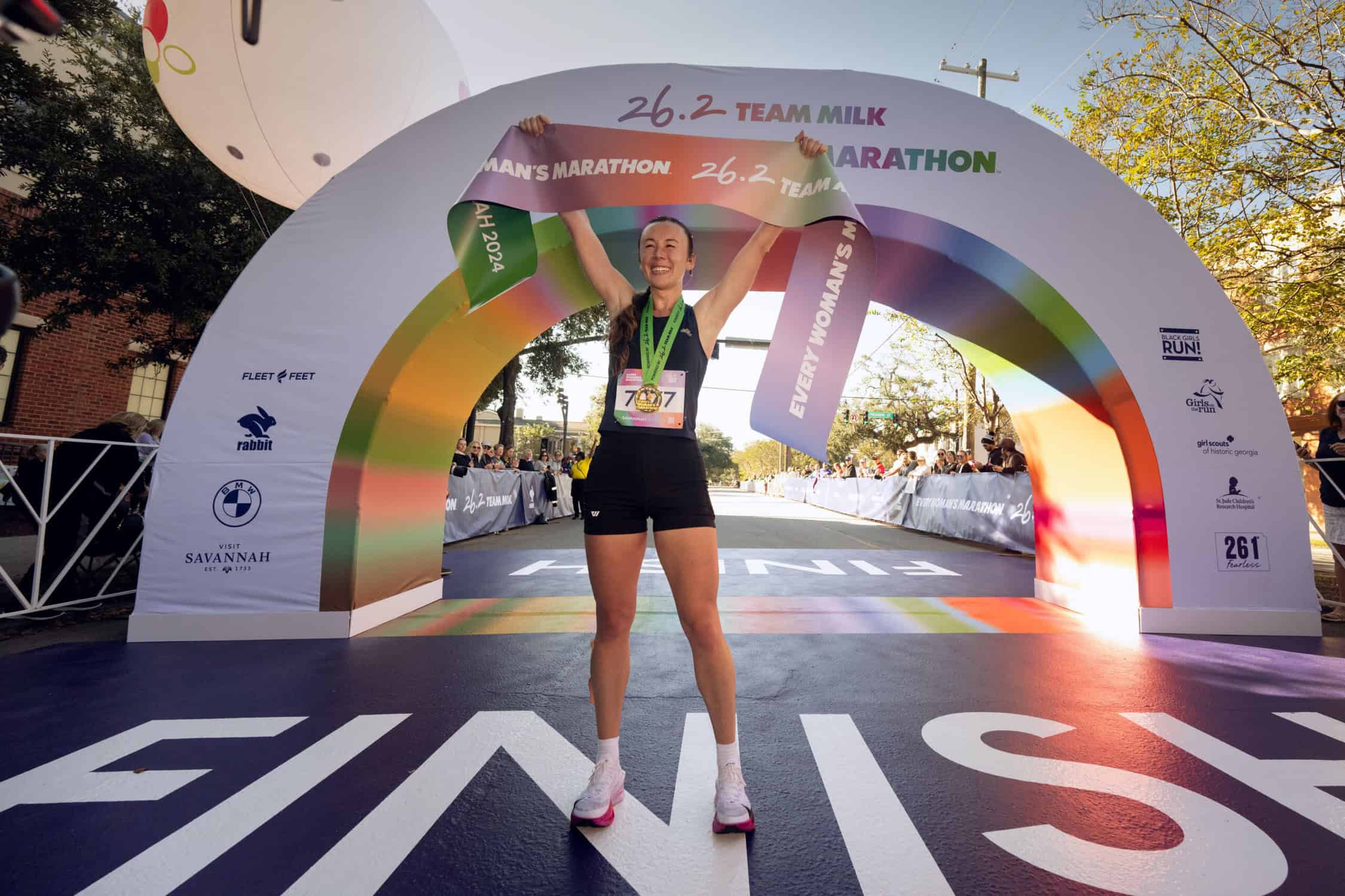 a runner who run the every woman's marathon holding a banner above her head at the finish line